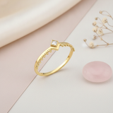 gold chevron ring with beaded edging and a single square clear stone, on cream fabric with dried flowers and a pink stone