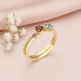 gold ring with magenta, deep red, and light blue gemstones in beaded bezels, on pink fabric with white flowers