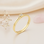gold ring with two offset square settings of clear stones, on cream fabric with dried flowers and a pink stone