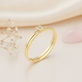 gold ring with two offset square settings of clear stones, on cream fabric with dried flowers and a pink stone
