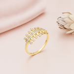 gold ring with a central row of pave-set squares flanked by textured gold pillars, on pink fabric with a dried flower