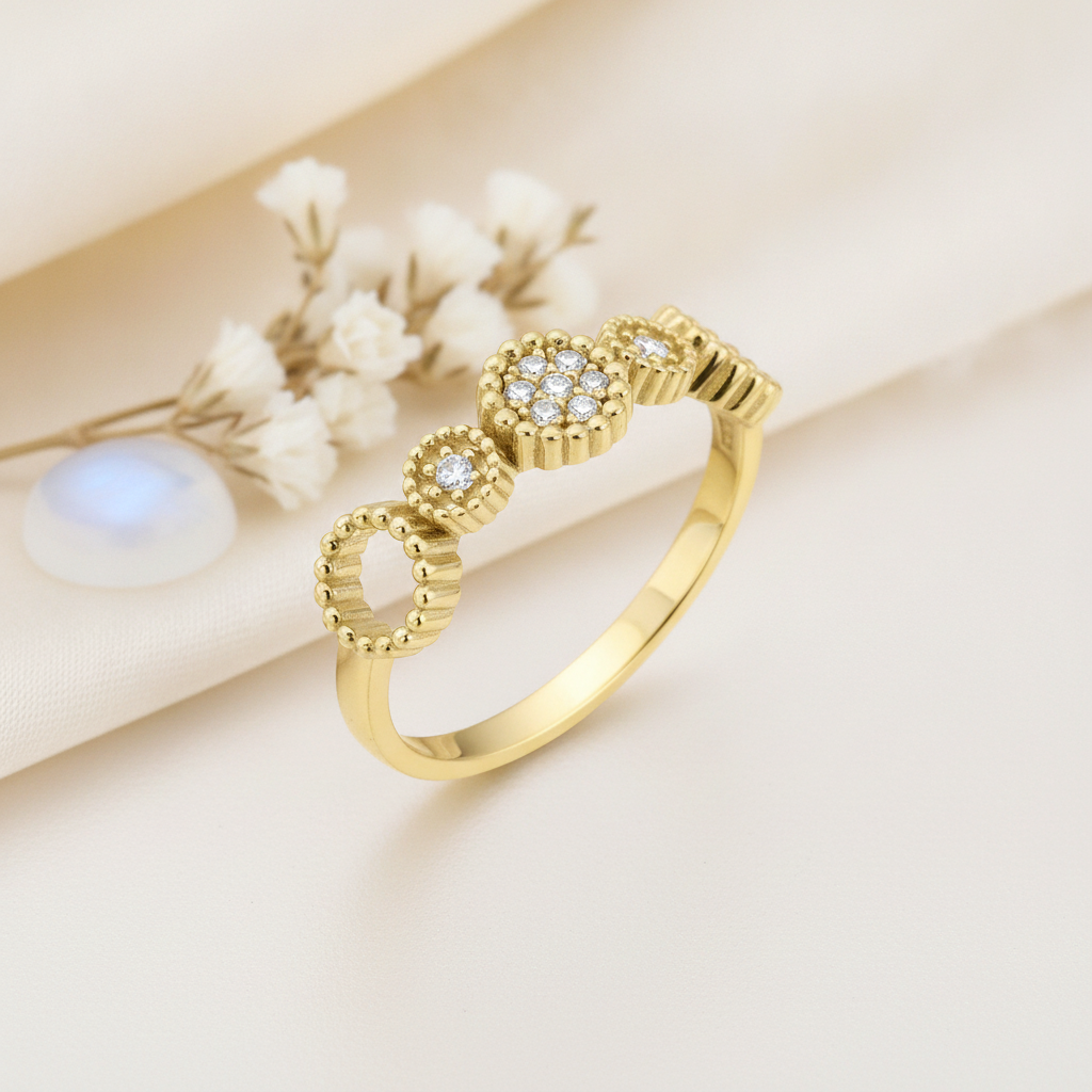 gold ring with a floral cluster of clear stones and textured beaded circles, on cream fabric with white flowers and a blue stone