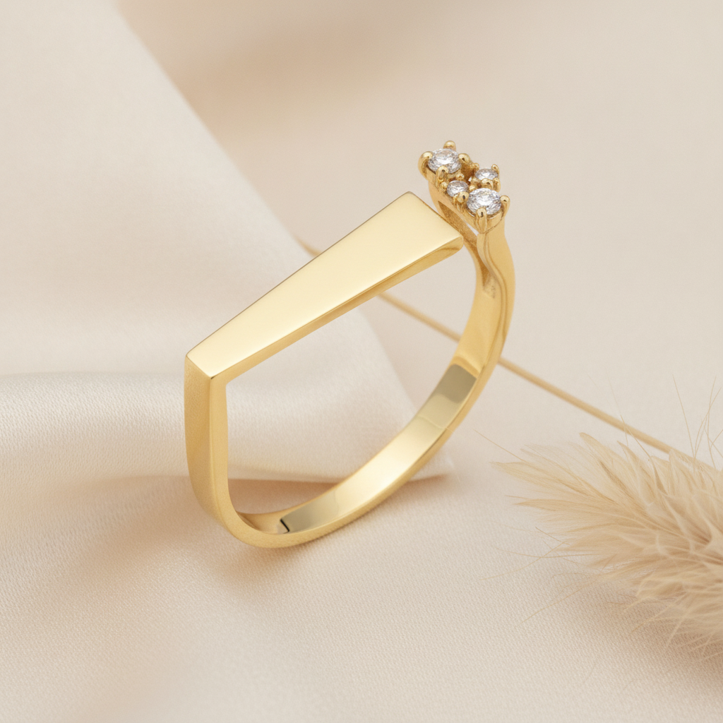 asymmetrical gold ring with a tapered bar and a cluster of clear stones, on cream fabric with a beige feather prop