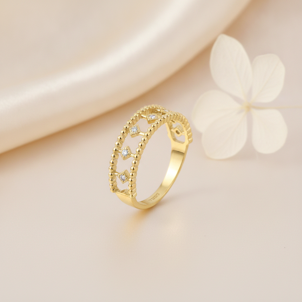 openwork gold ring with double beaded borders and kite-shaped stone settings, on cream fabric with a white flower
