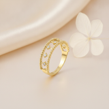 openwork gold ring with double beaded borders and kite-shaped stone settings, on cream fabric with a white flower