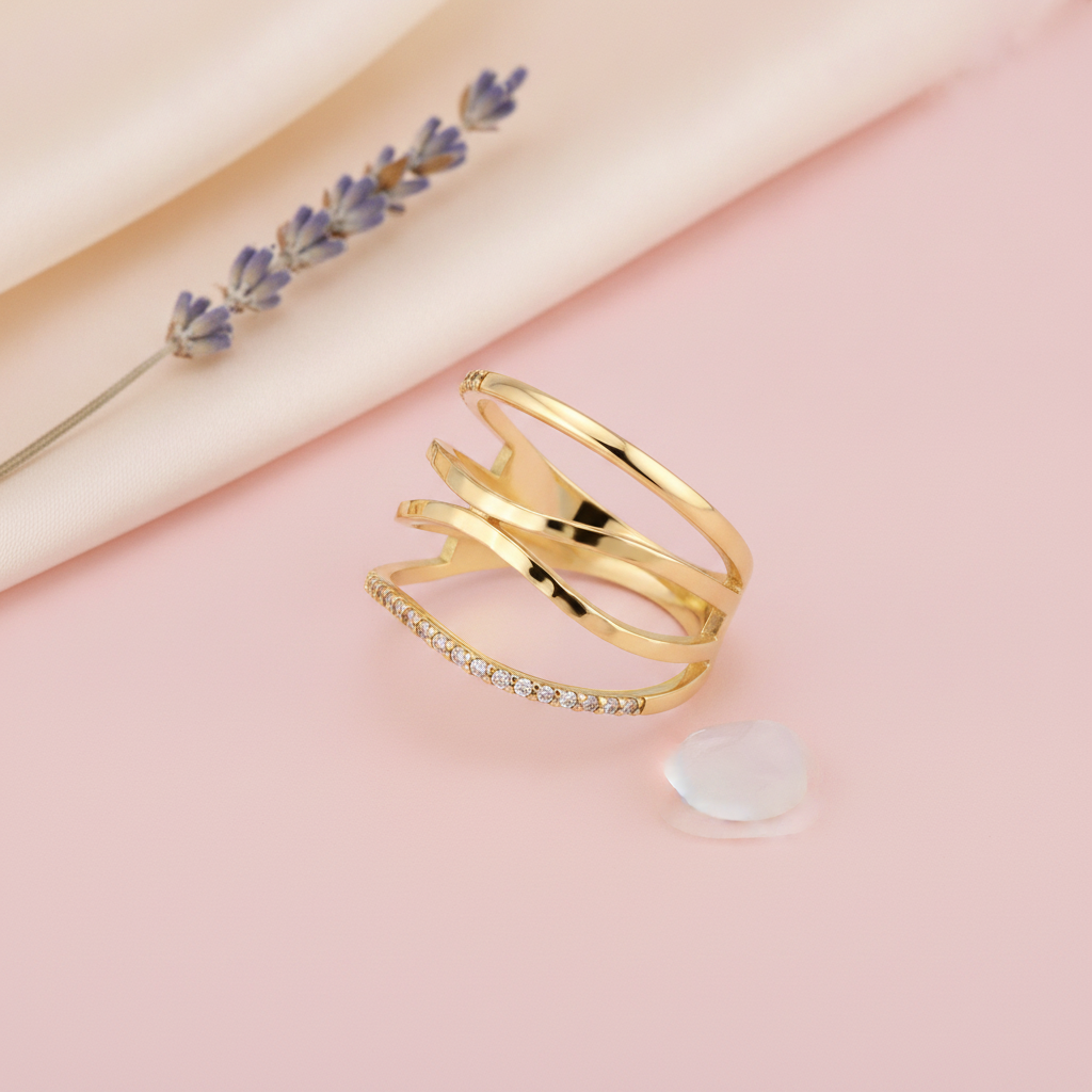 wide gold ring with layered openwork arcs and small clear stones, on pink fabric with dried roses