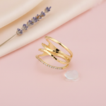 wide gold ring with layered openwork arcs and small clear stones, on pink fabric with dried roses