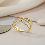 gold crossover ring with two rows of pave-set clear stones, on pink fabric with a eucalyptus leaf