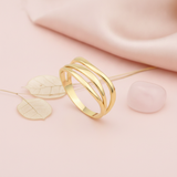 gold ring with three smooth sweeping bands and open space between, on cream fabric with a rose and dried leaves