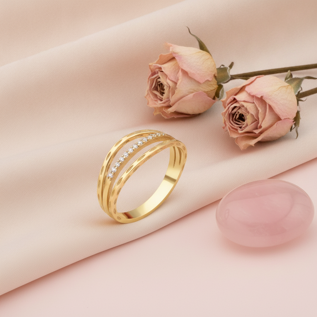 triple-band gold ring with a row of clear stones framed by textured arches, on pink fabric with dried roses