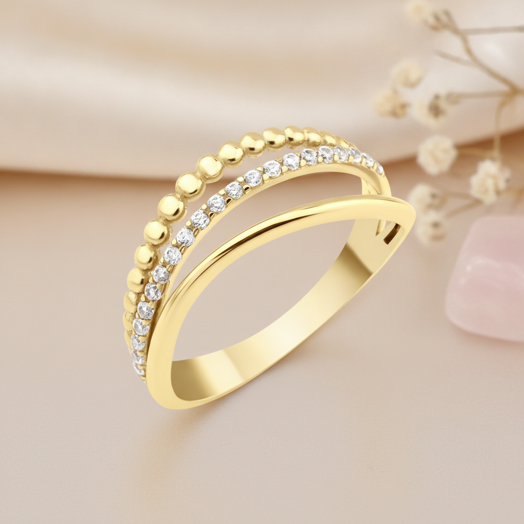 gold crossover ring with a beaded row and a row of pave clear stones, on blush fabric with dried flowers