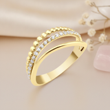 gold crossover ring with a beaded row and a row of pave clear stones, on blush fabric with dried flowers