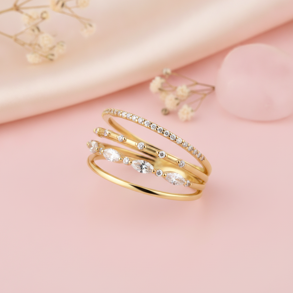 multi-band gold ring with pave, round, and marquise clear stones, on pink fabric with dried flowers and a pink stone