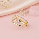 multi-band gold ring with pave, round, and marquise clear stones, on pink fabric with dried flowers and a pink stone