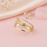 multi-band gold ring with pave, round, and marquise clear stones, on pink fabric with dried flowers and a pink stone