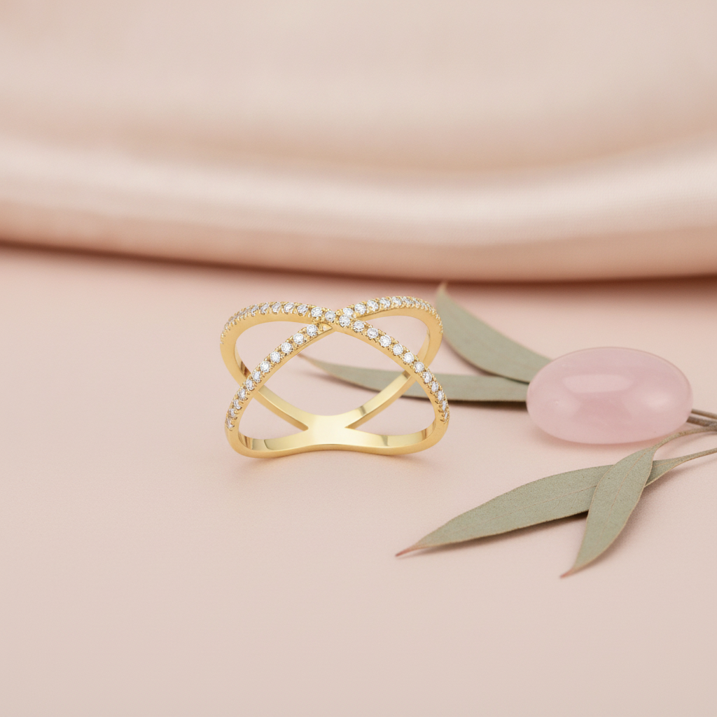 gold X-shaped crossover ring paved with clear stones, on pink fabric with a eucalyptus leaf and pink stone
