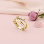 triple-band gold ring with an asymmetrical trail of clear stones, on pink fabric with a peony flower