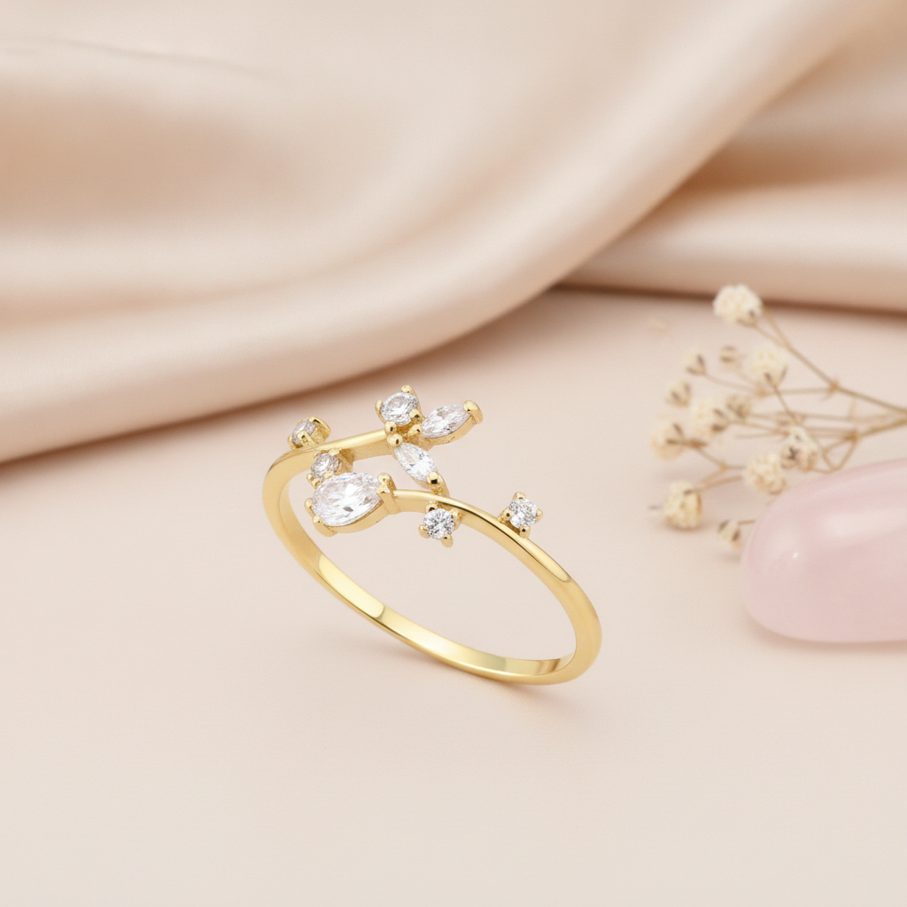 asymmetric gold bypass ring with a cluster of pear, marquise, and round clear stones, on cream fabric with a pinecone flower