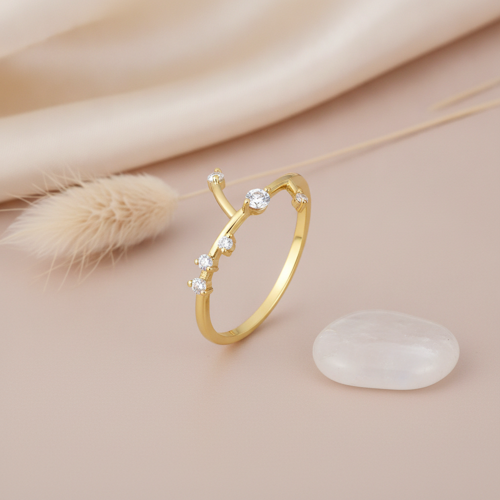 open twig-inspired gold ring with scattered clear stones along branching stems, on cream fabric with a dried flower