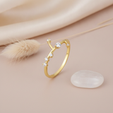 open twig-inspired gold ring with scattered clear stones along branching stems, on cream fabric with a dried flower