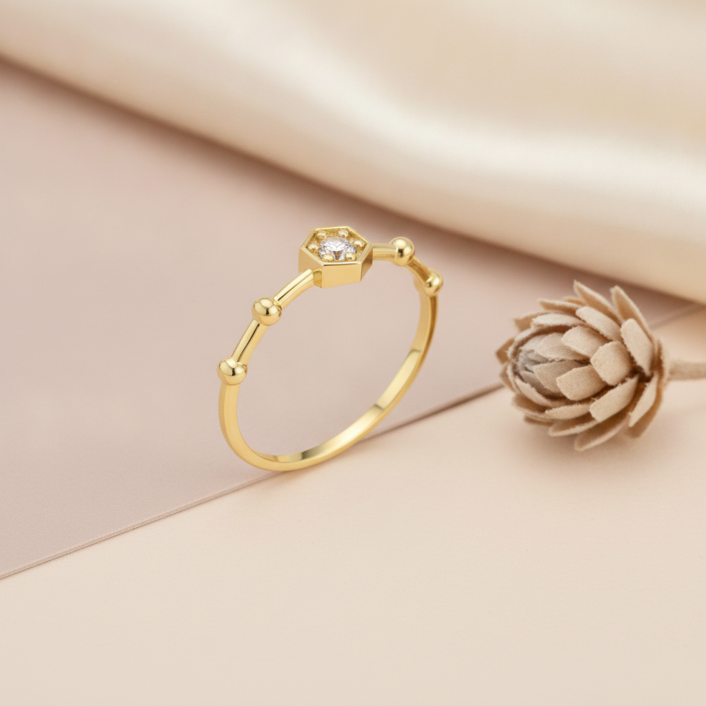 gold ring with a hexagonal bezel stone and small raised gold beads, on cream fabric with a dried flower
