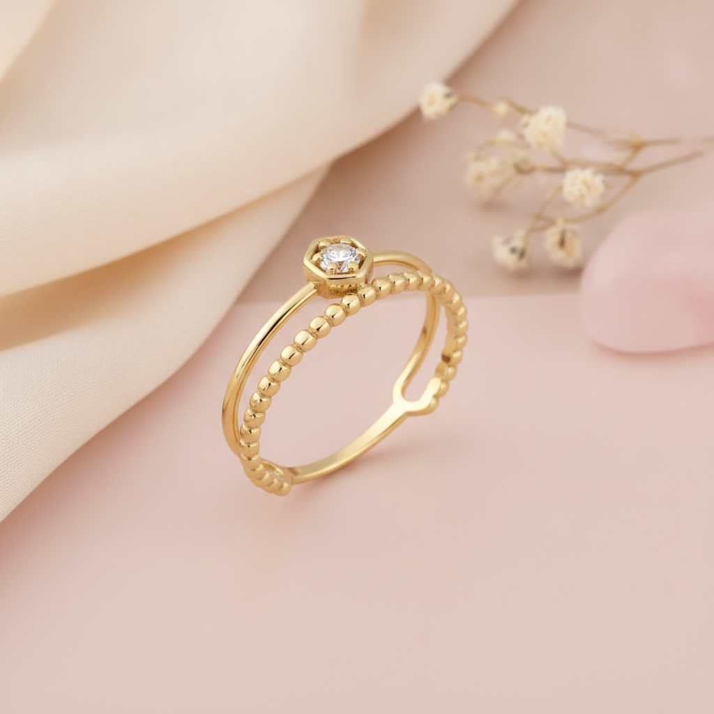 gold ring with a smooth band and a beaded band joined by a hexagonal bezel stone, on cream fabric with a dried flower