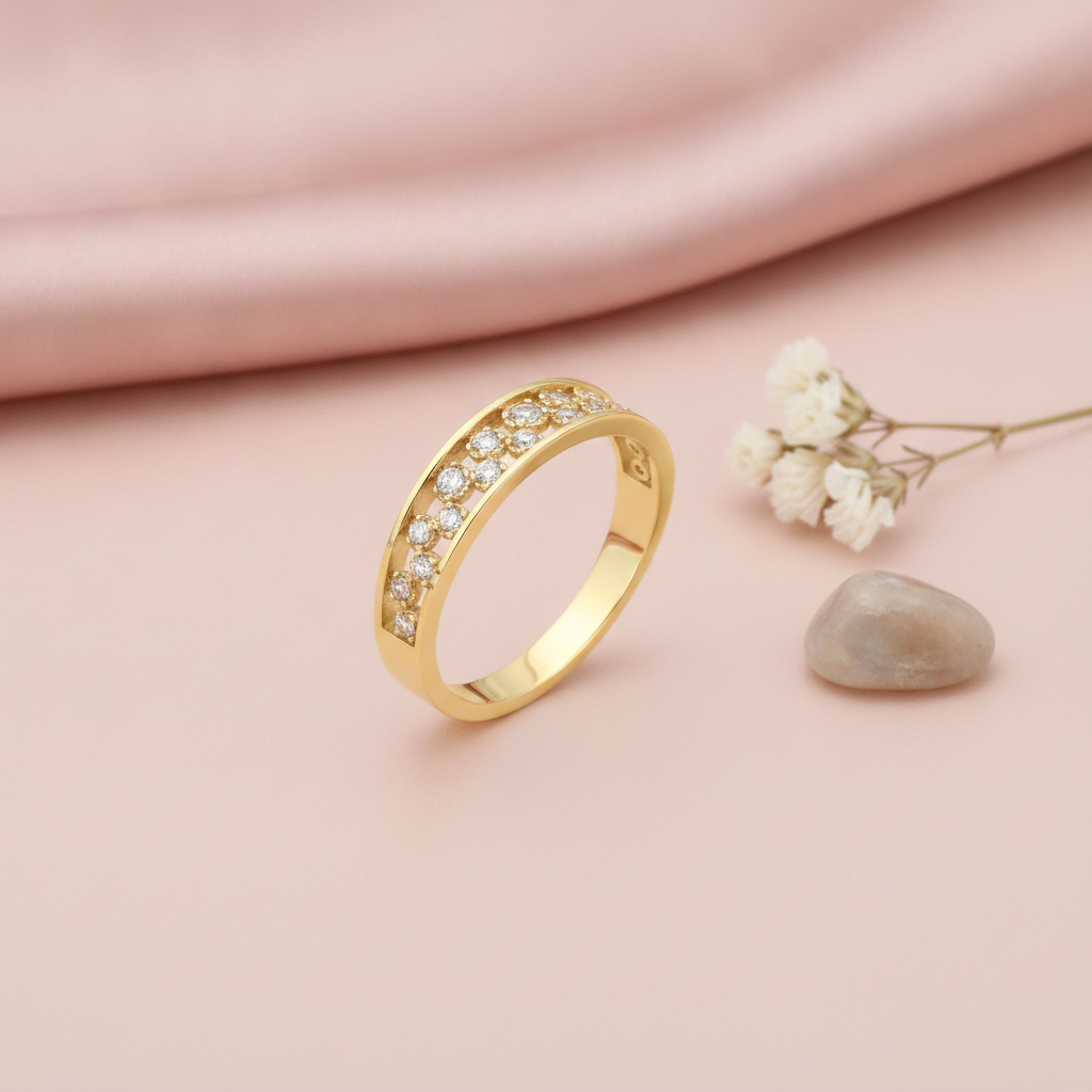 gold ring with two rows of pave clear stones between polished edges, on pink fabric with a dried flower and stone