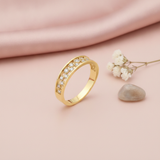 gold ring with two rows of pave clear stones between polished edges, on pink fabric with a dried flower and stone