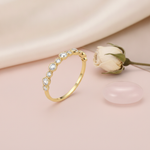 slender gold ring with alternating size clear stones in beaded bezels, on cream fabric with a dried flower and stone