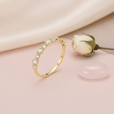 slender gold ring with alternating size clear stones in beaded bezels, on cream fabric with a dried flower and stone