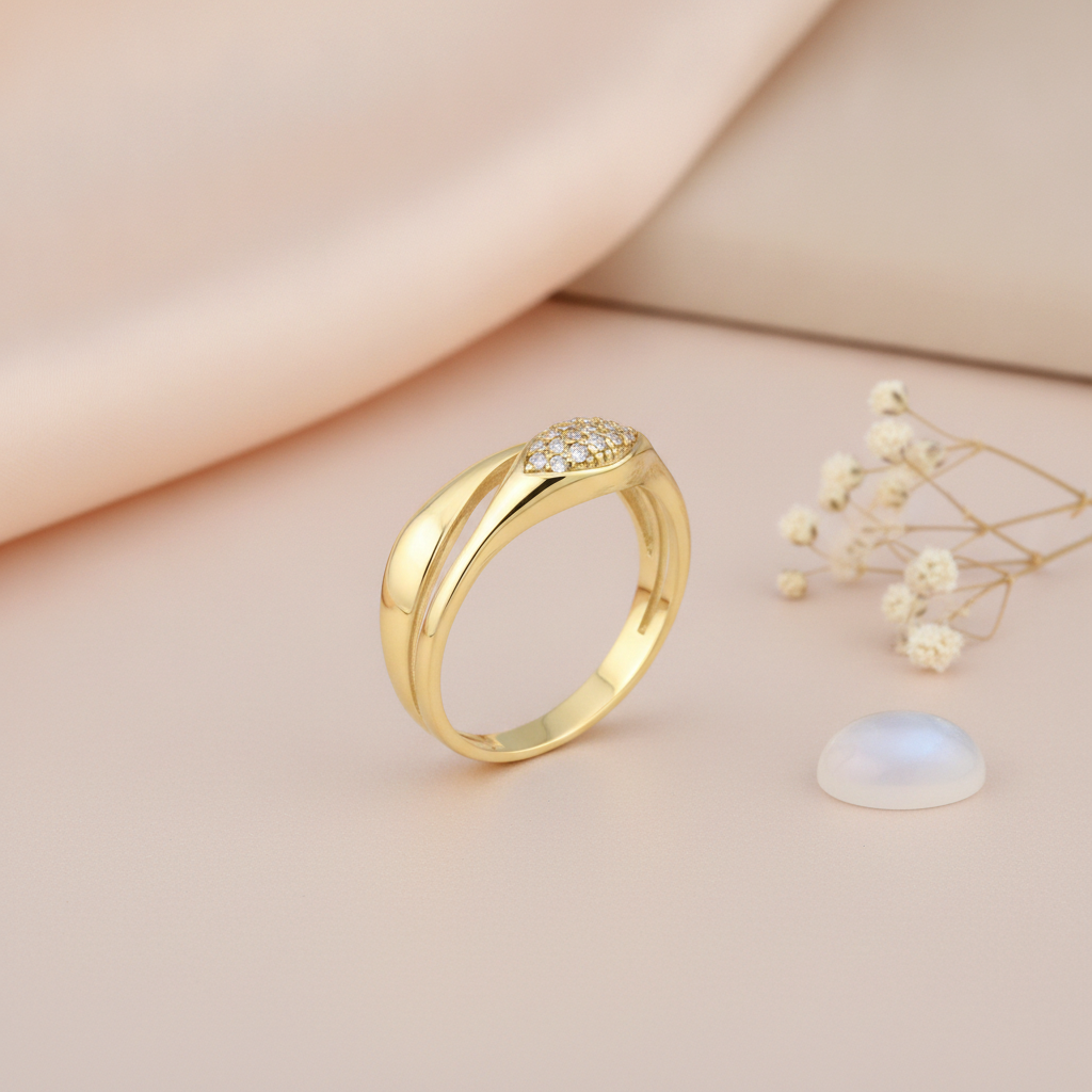sculpted gold bypass ring with an eye-shaped cluster of clear stones, on cream fabric with a white flower and stone