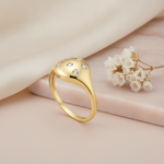 gold dome ring with scattered flush-set clear stones, on cream fabric with a dried flower