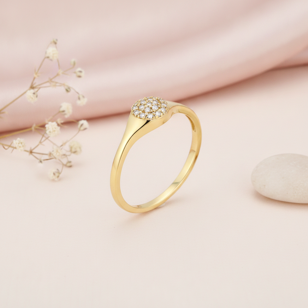 gold signet ring with a circular pave stone crest, on cream fabric with a dried flower