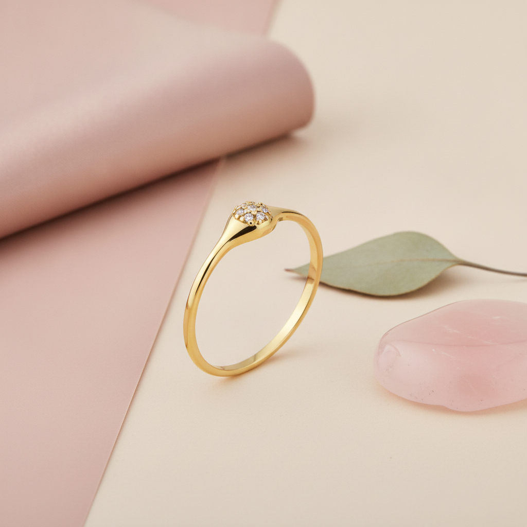 gold signet ring with a small circular crest of clear stones, on cream fabric with a rose quartz stone