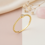 textured gold beaded band ring with a round stone cluster on a two-tone blush and cream background with dried flowers