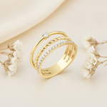 three-strand gold ring combining a pave row, a twisted rope, and a solitaire stone on cream fabric with dried flowers