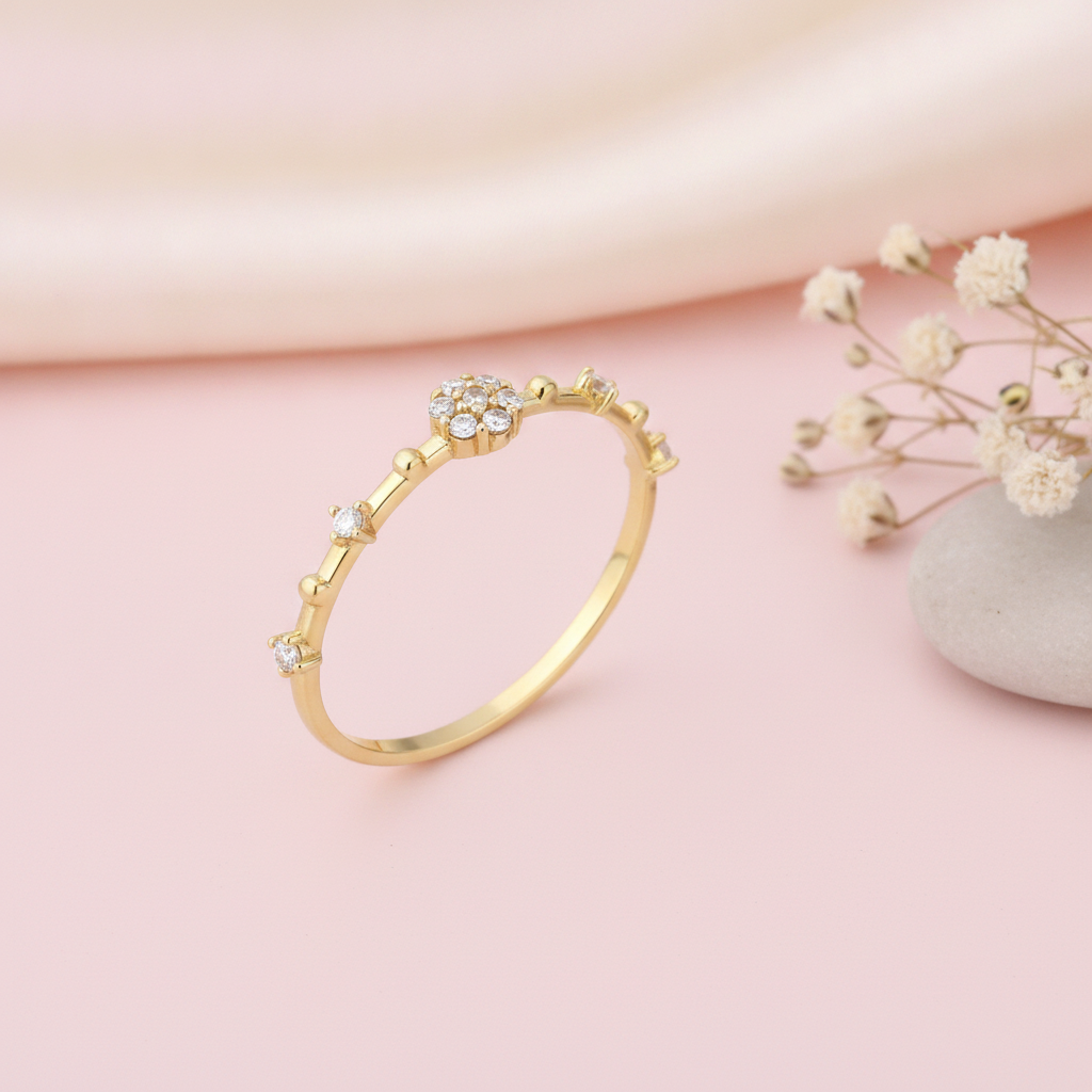 slender gold ring with a floral stone cluster and scattered accent stones on pink silk with dried flowers and a pebble