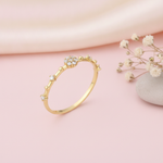 slender gold ring with a floral stone cluster and scattered accent stones on pink silk with dried flowers and a pebble