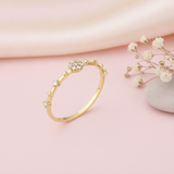 slender gold ring with a floral stone cluster and scattered accent stones on pink silk with dried flowers and a pebble