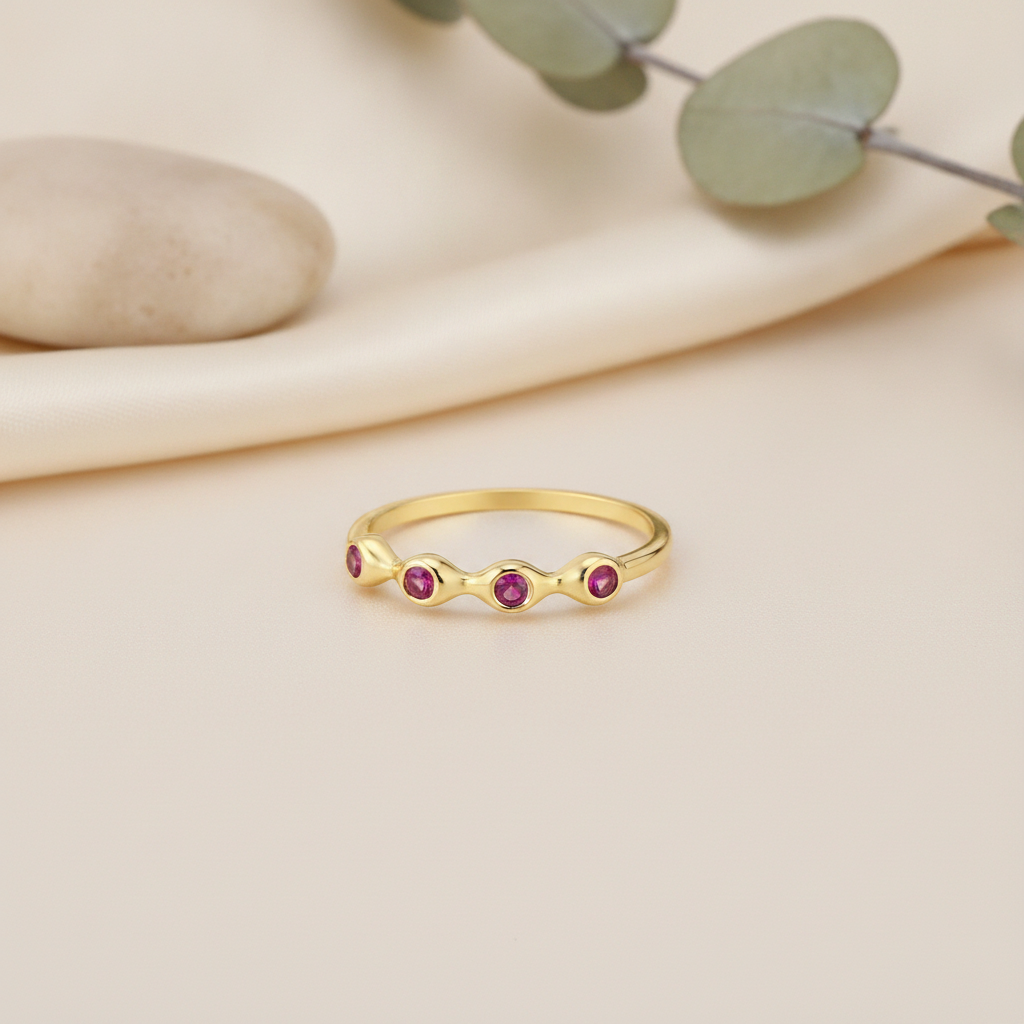 wavy gold ring with five pink stones on cream fabric with a smooth pebble and eucalyptus sprig