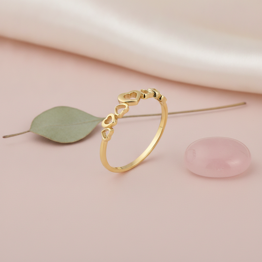 gold ring with a graduating row of open heart cutouts on pink silk with a green leaf and a rose quartz stone