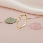gold ring with a graduating row of open heart cutouts on pink silk with a green leaf and a rose quartz stone