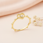 gold ring with an open heart outline and a single clear stone on pink silk with a eucalyptus leaf and rose quartz stones