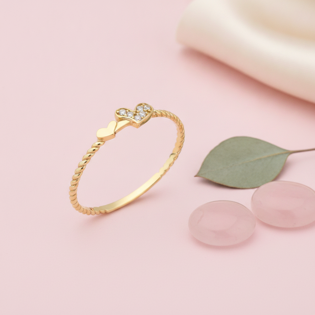 gold ring on a twisted rope band with a plain heart beside a pave heart on pink silk with a eucalyptus leaf and rose quartz stones