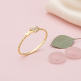 gold ring on a twisted rope band with a plain heart beside a pave heart on pink silk with a eucalyptus leaf and rose quartz stones