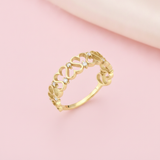 openwork gold ring with interlocking curves and small clear stones on a blush pink background with satin drape