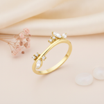 gold ring with a curved silhouette set with marquise and round clear stone clusters on cream silk with blush flowers