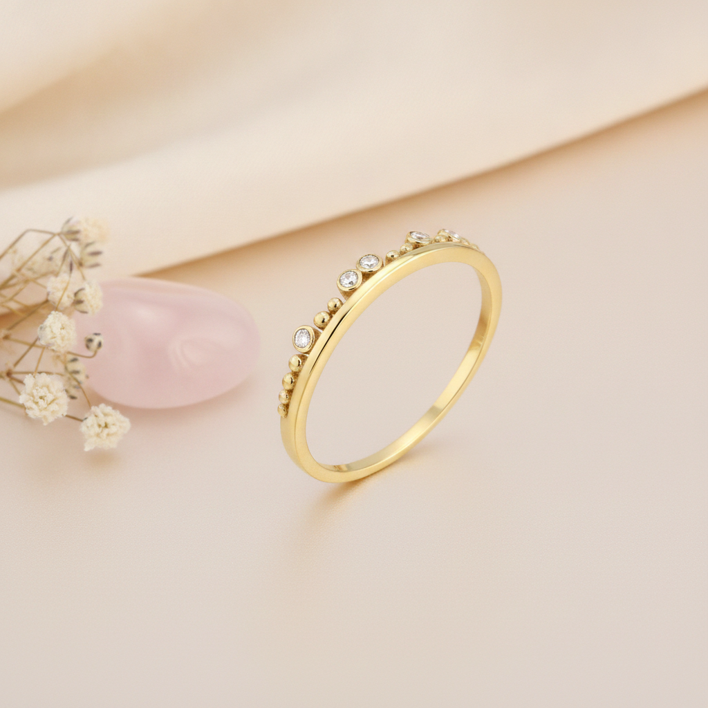 gold ring with an arched crest of polished beads and five bezel-set clear stones on blush silk with dried flowers