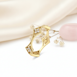 sculptural gold ring with beaded arches, clear stone clusters, and openwork filigree on a white background with pink silk drape and dried flowers
