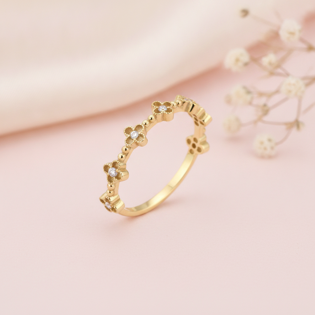 gold ring with four-petaled floral motifs and clear center stones along the band on blush silk with dried flowers